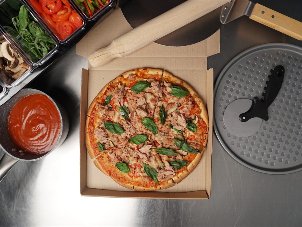 Overhead view of a tuna and basil pizza boxed on a stainless prep bench, a menu application for 555 Tuna Flakes