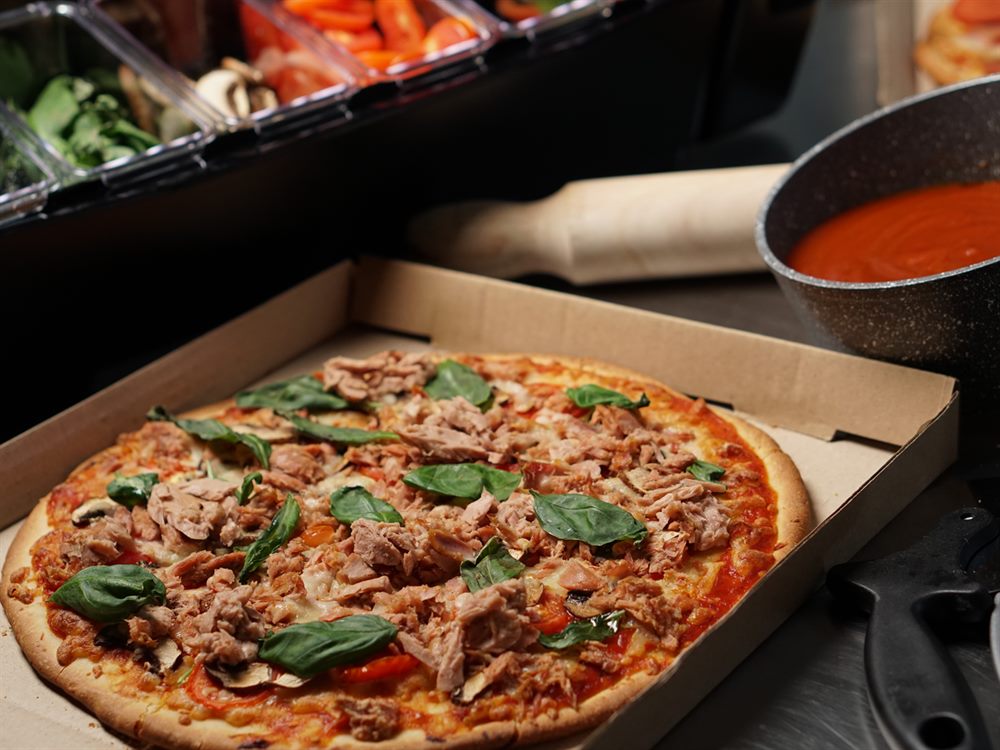 Tuna and basil pizza boxed beside a pan of pizza sauce and a topping rail, a menu application for Blue Bay Tuna Flakes in Oil