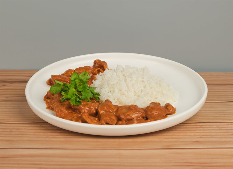 Buttered chicken in a spiced tomato and coconut milk sauce, plated with rice and a cilantro sprig for food service