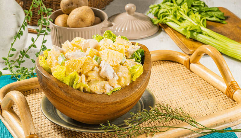 Chicken potato salad in a wooden bowl lined with lettuce, with potatoes and celery behind it