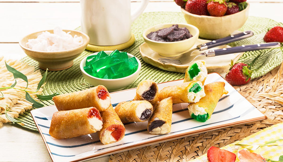 Fried dessert lumpia cut open to show strawberry, ube and buko pandan fillings, on a striped platter