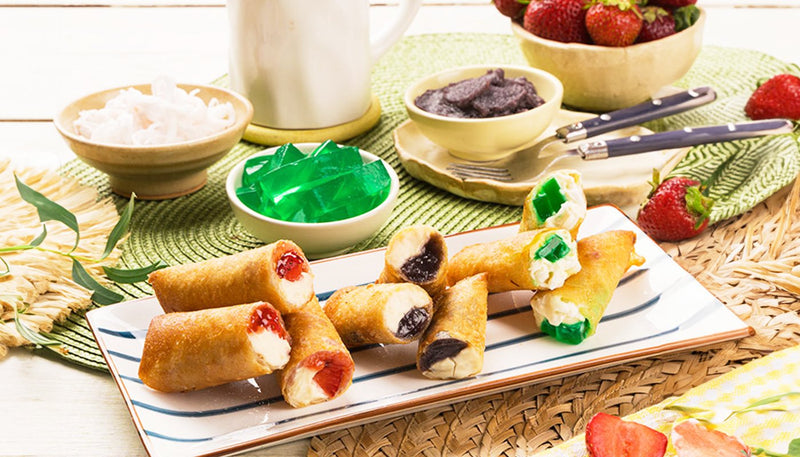 Fried dessert lumpia cut open to show strawberry, ube and buko pandan fillings, on a striped platter