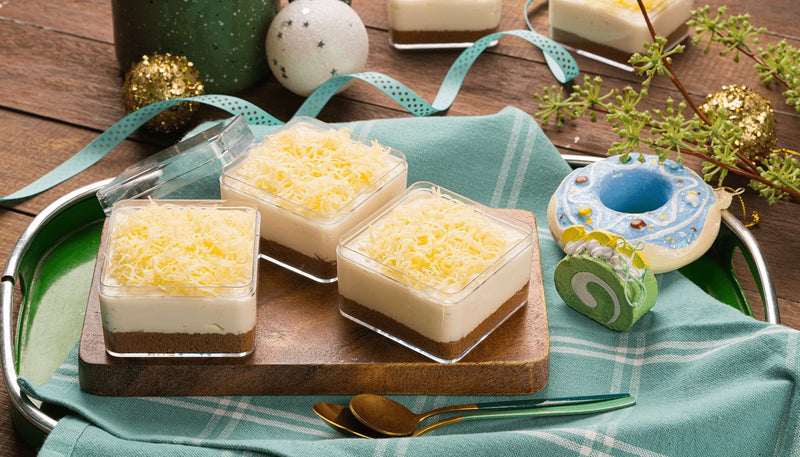 Three no bake queso de bola cheesecake cups with graham crust and grated cheese on top, on a wooden board