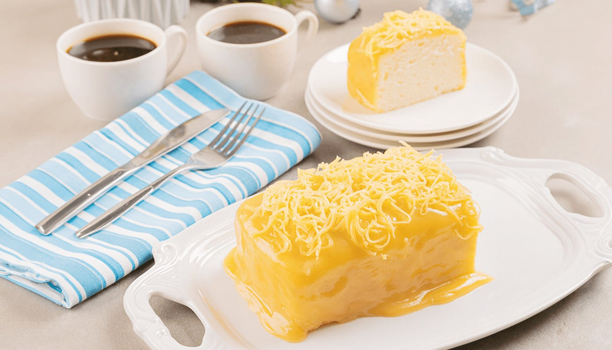 No bake yema cake topped with grated cheddar on a white serving tray, with a cut slice and two cups of coffee behind it