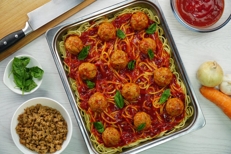 Filipino-style spaghetti with meatballs in a food service tray, finished with basil and tomato sauce