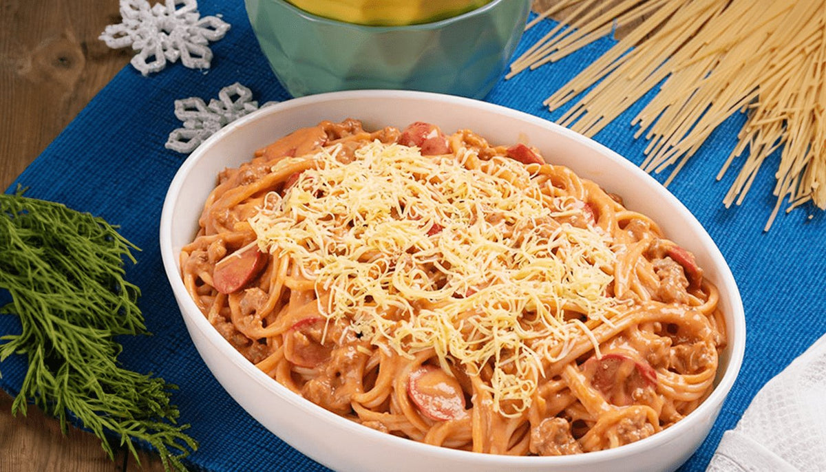 Sweet style spaghetti with hotdog slices and grated cheese in a white oval dish, with dry spaghetti behind it