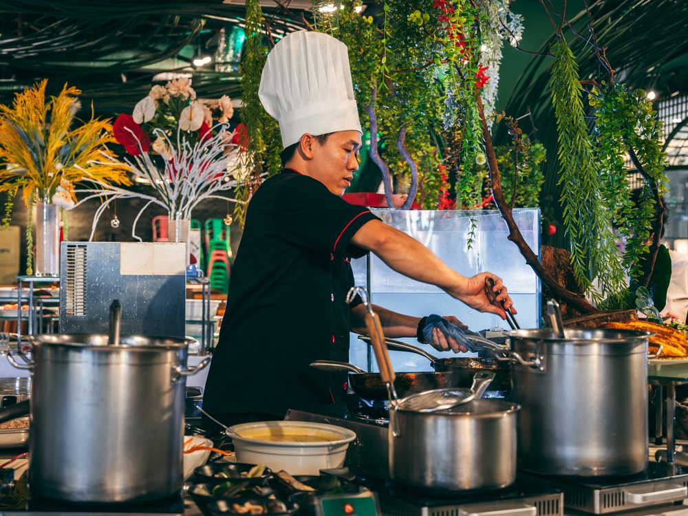 A chef tending a wok and large stockpots at a hotel buffet cooking station