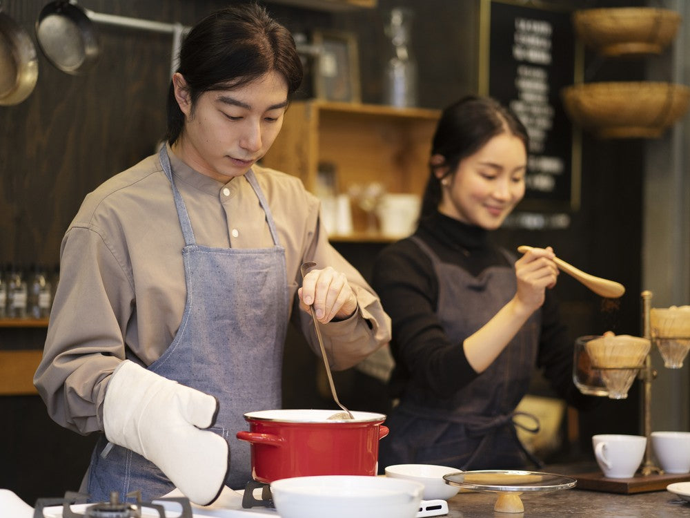 Two cooks preparing a dish together on a stovetop in a restaurant kitchen